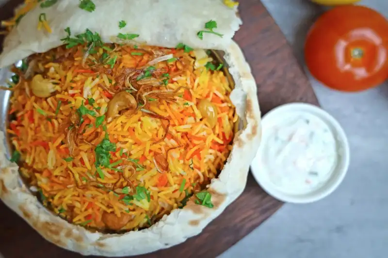 Close-up of biryani being layered in a copper pot