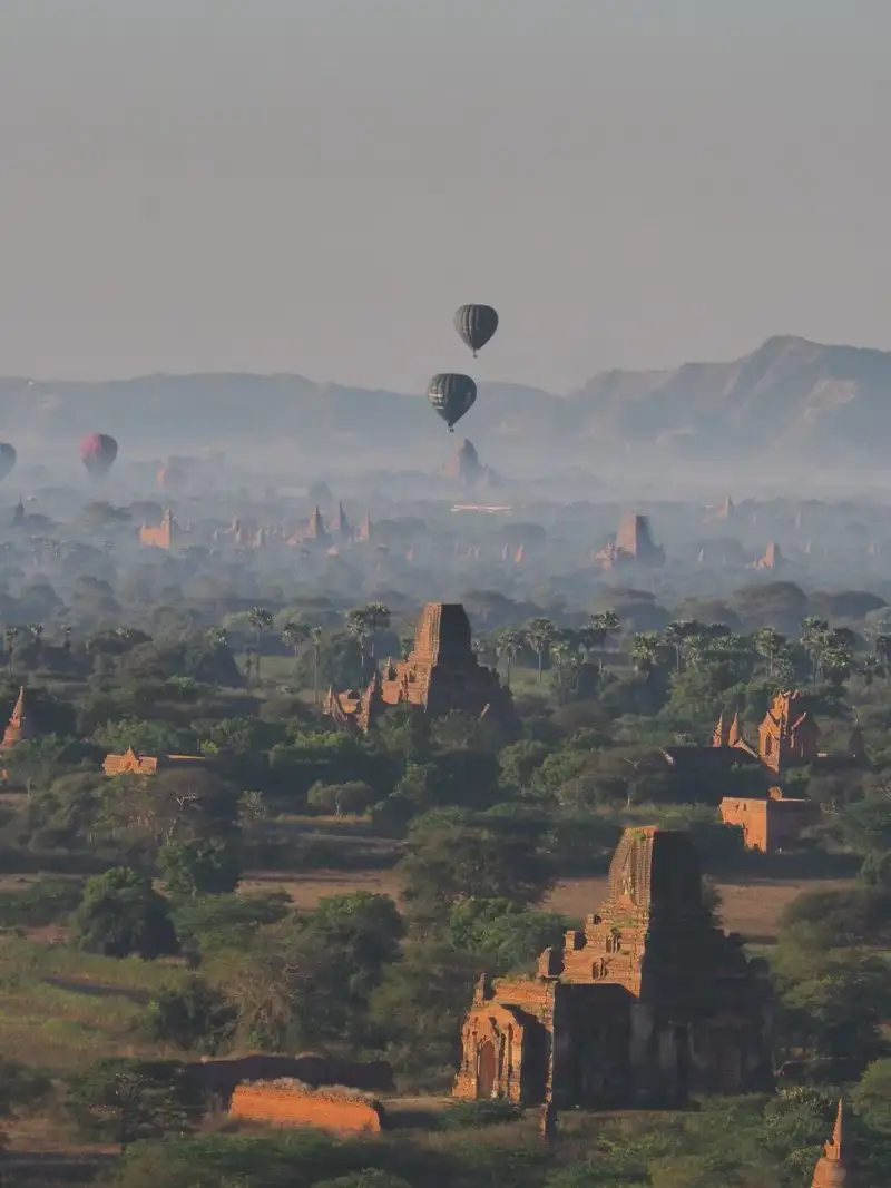 Vue aérienne d'anciens temples de Bagan au lever du soleil avec des ballons à air chaud au loin