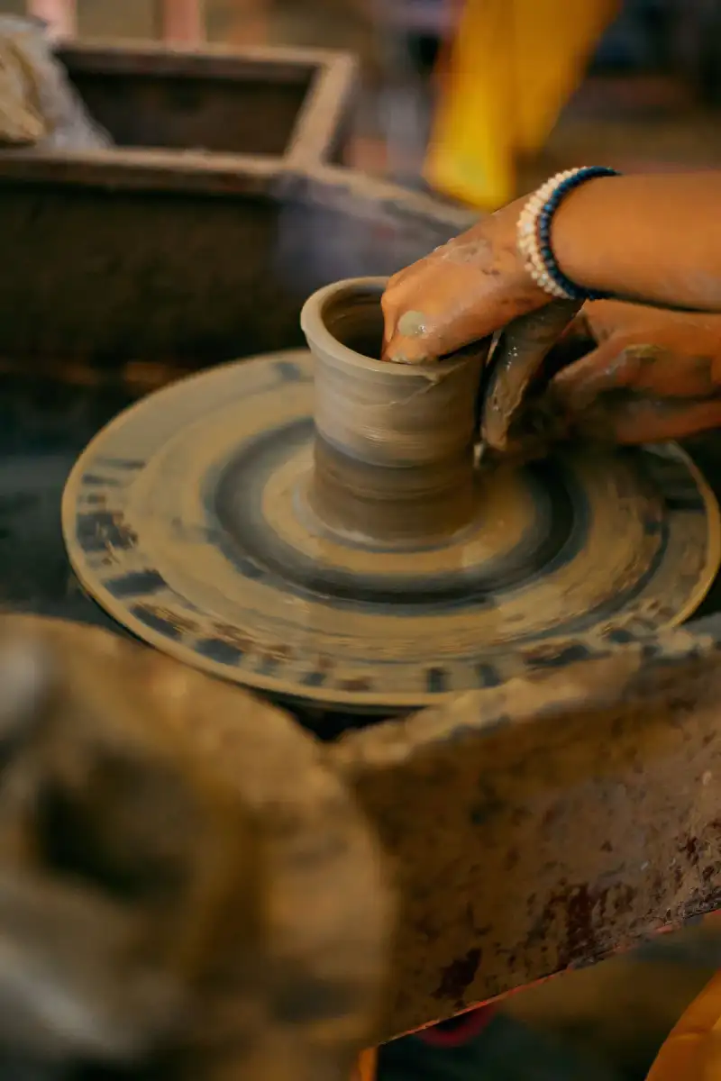 An experienced Rishtan pottery artisan meticulously painting intricate blue patterns onto a ceramic bowl in a traditional workshop, surrounded by raw clay and finished pieces