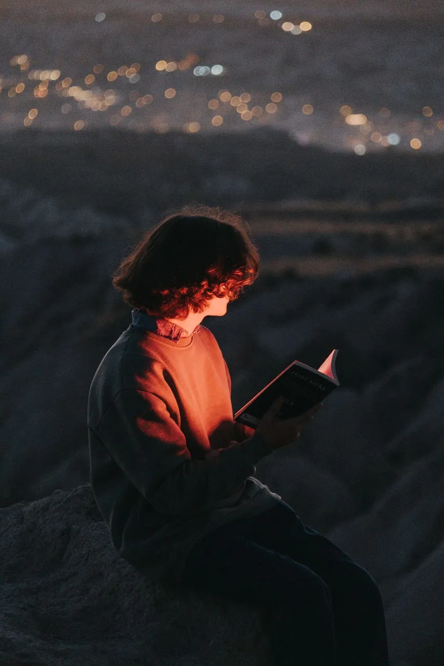 Person reading a glowing book in a dark room with magical particles floating