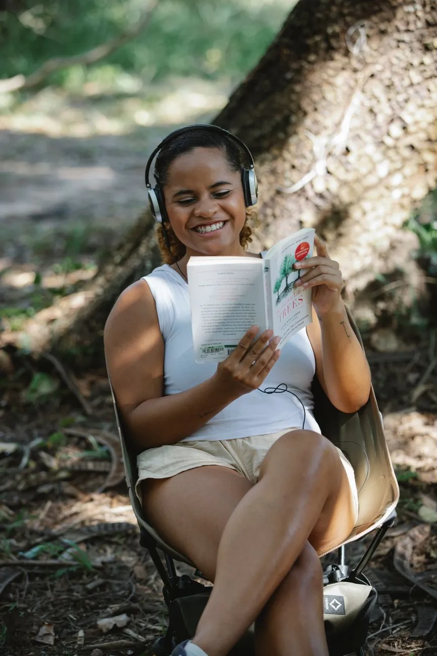 Person wearing noise cancelling headphones while reading a book in a park