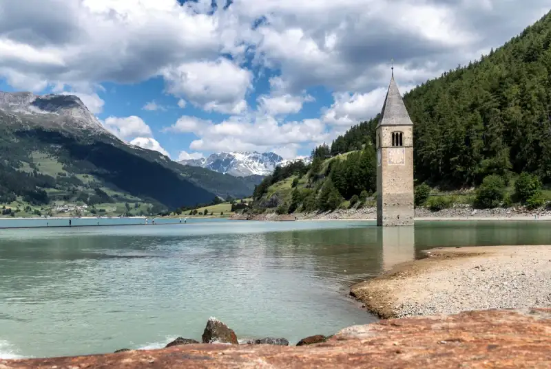 The ancient bell tower of Curon emerging from the blue waters of Lake Reschen against the Alpine backdrop