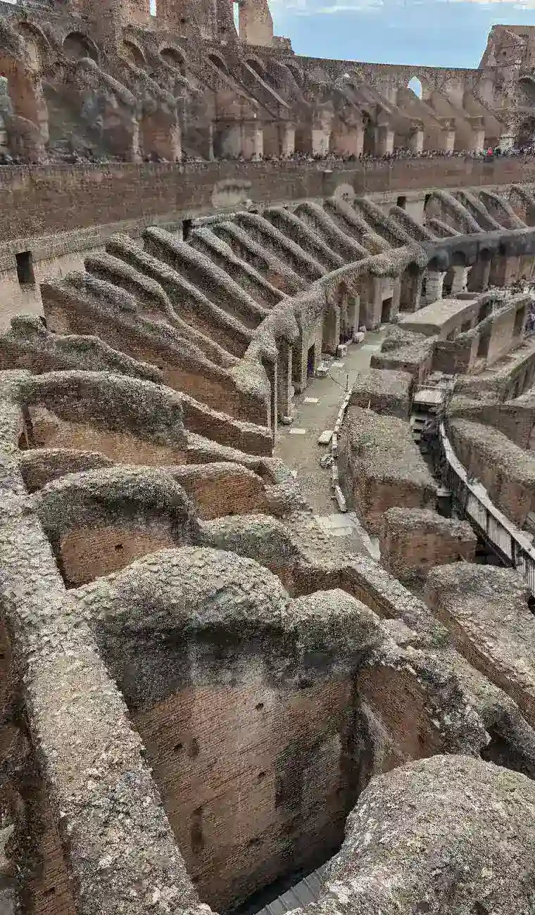 High angle shot of the Colosseum's interior ruins, intricate arches and tiers, ancient Roman engineering marvel, natural lighting, a lone tourist, sense of scale and history