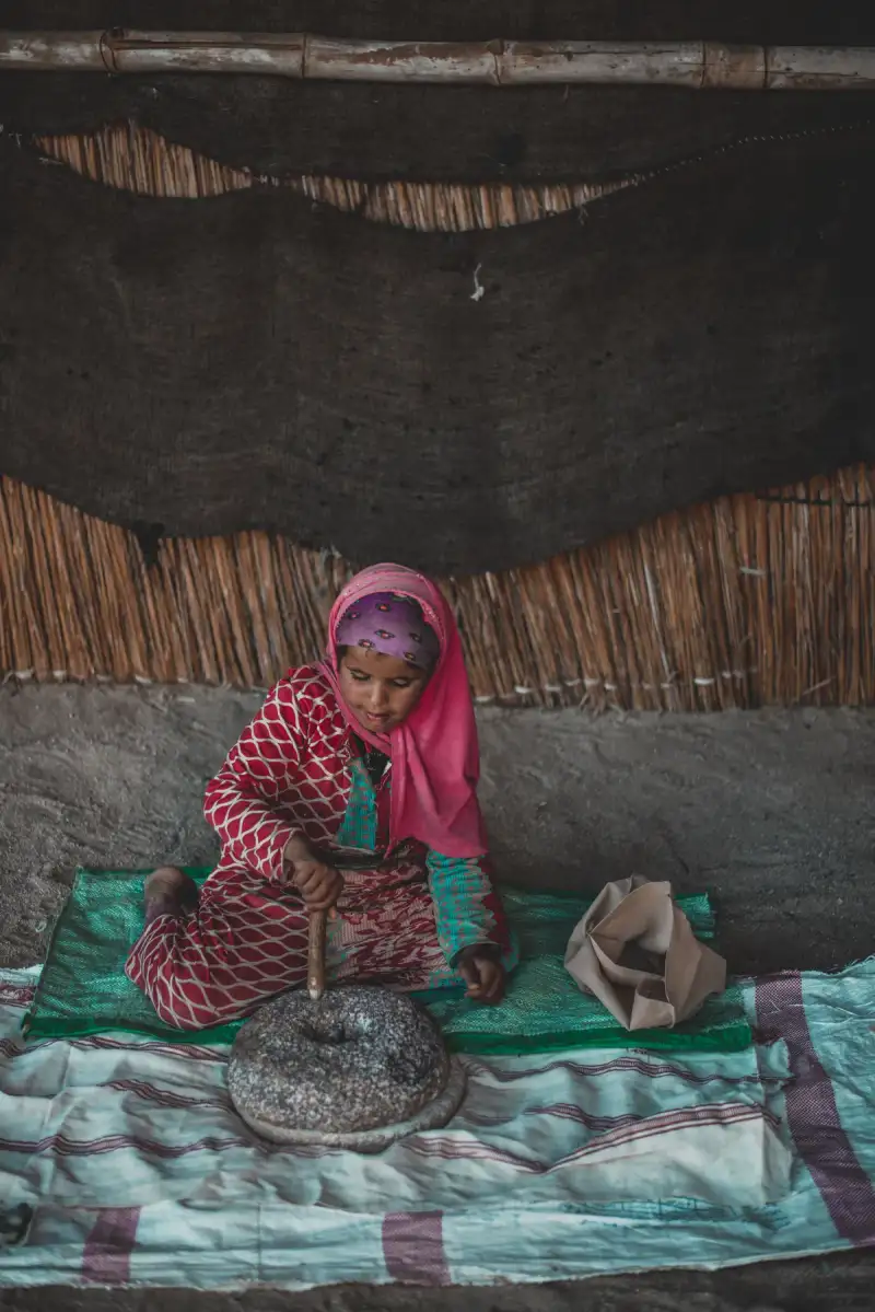 Traditional Peruvian woman grinding fermented quinoa on a stone metate, surrounded by ancient pottery