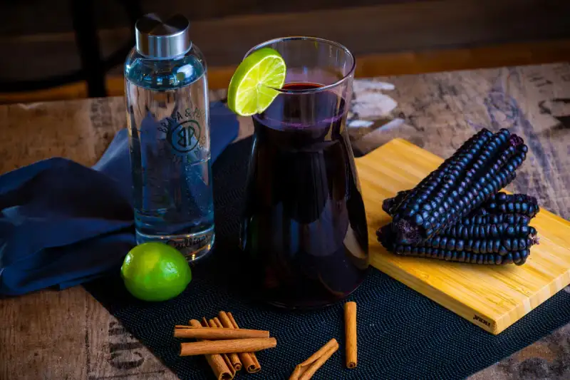 Close up of vibrant purple corn chicha beverage in a rustic traditional clay cup, with blurred Andean textiles in background