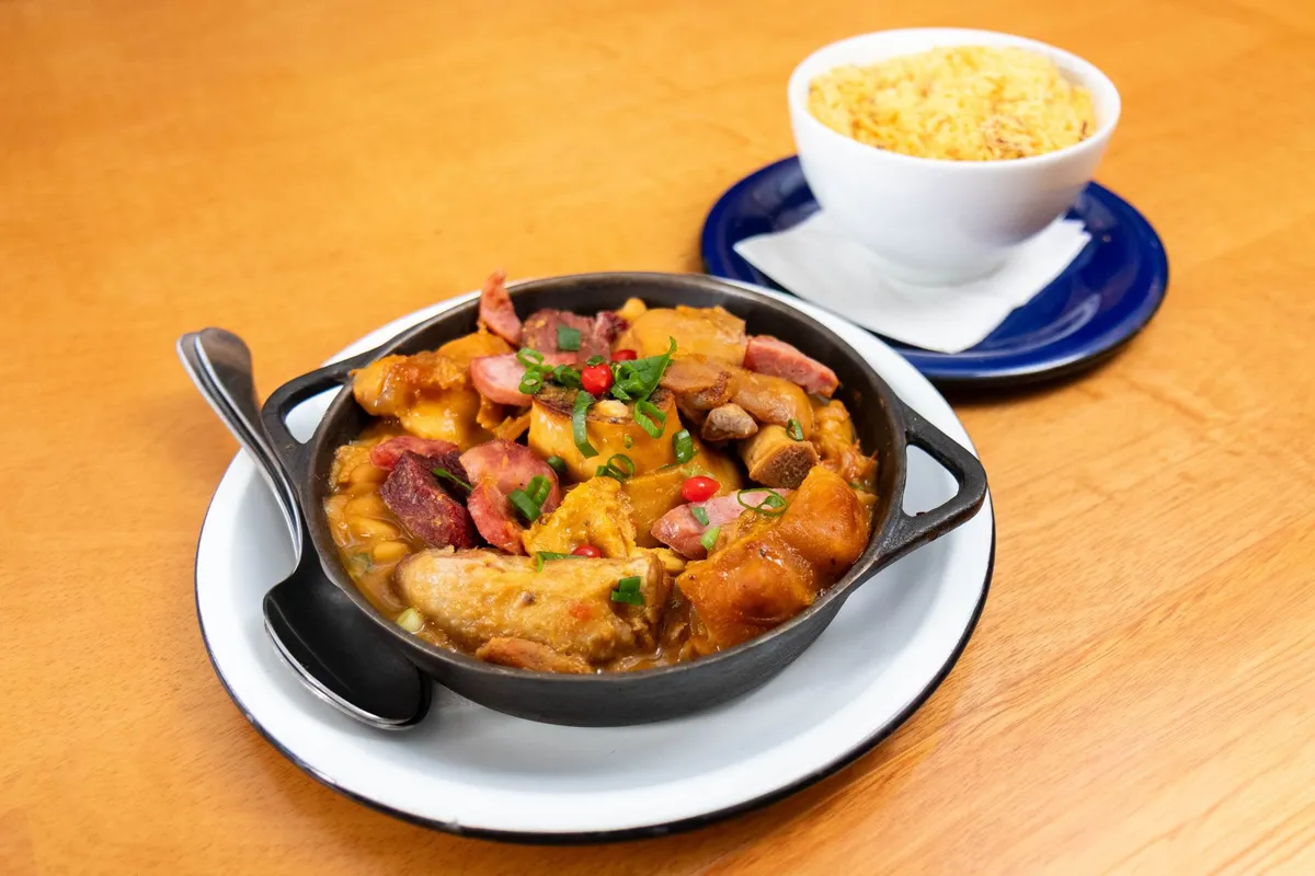 A colorful plate of feijoada served with rice, farofa, collard greens, and orange slices