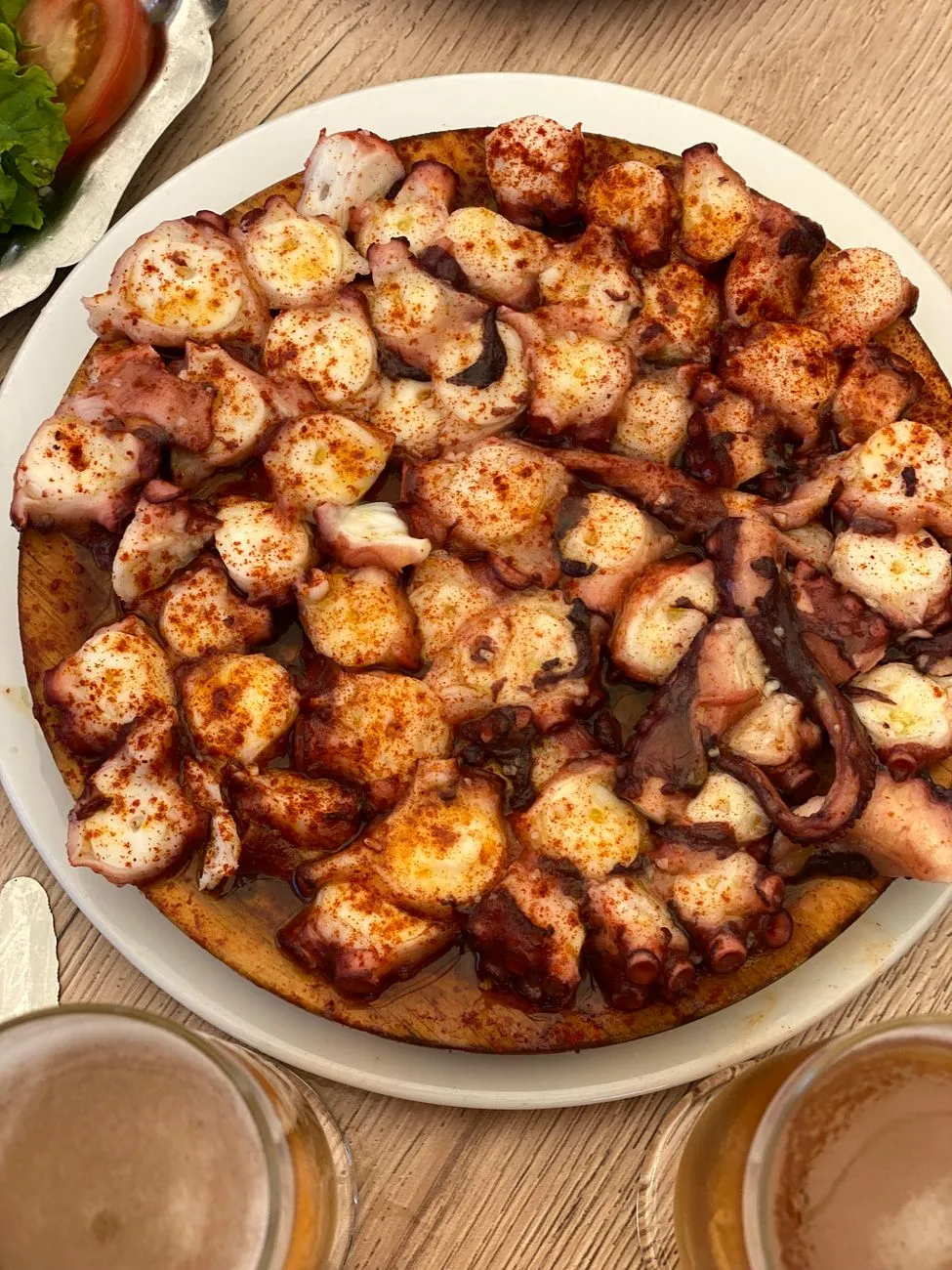 A wooden platter of sliced octopus sprinkled with paprika and olive oil