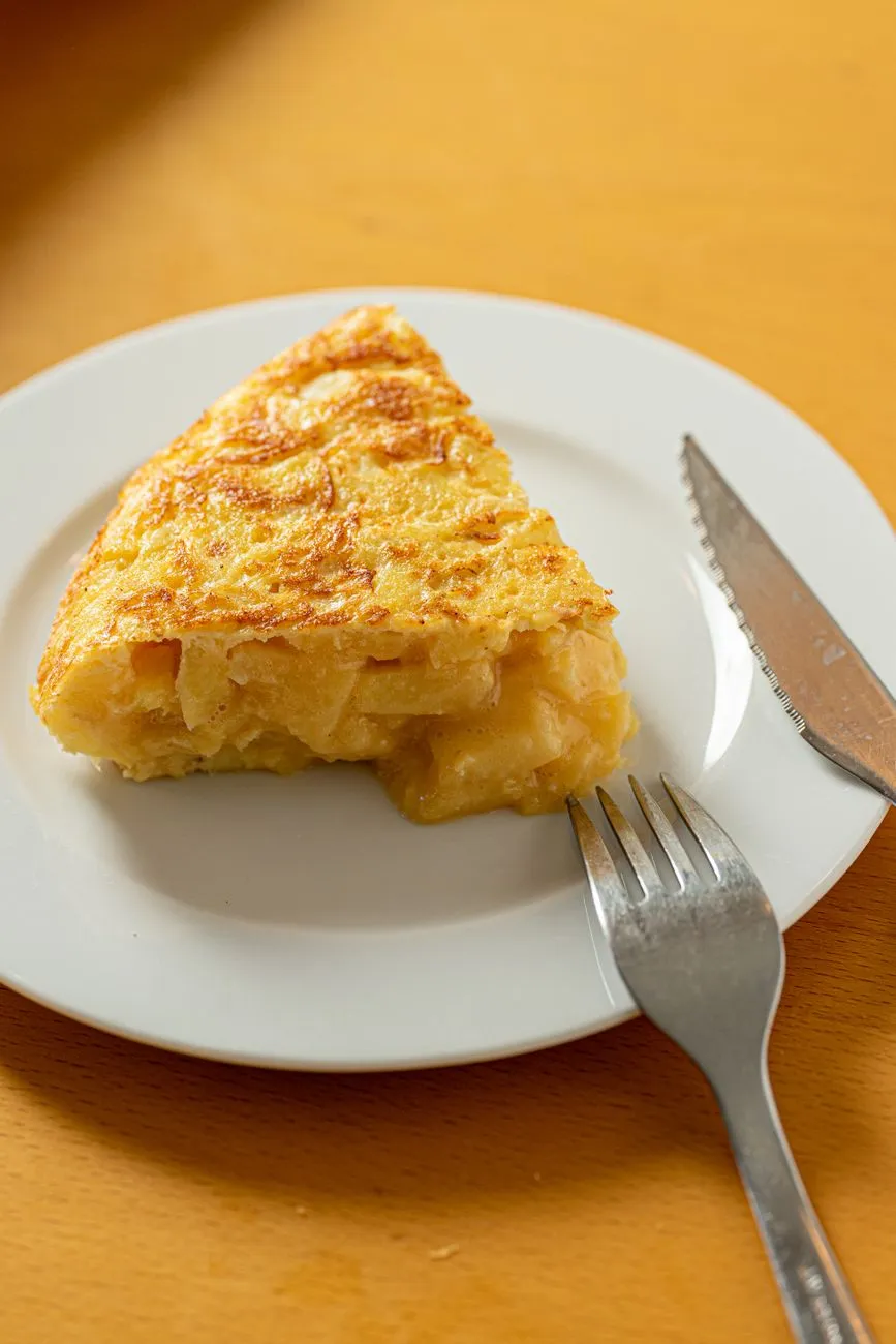A wedge of golden tortilla española on a white plate with a fork