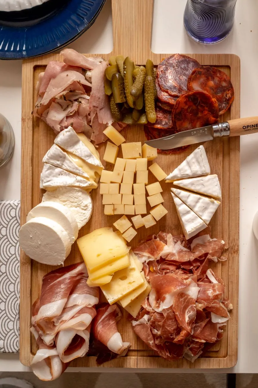 A wooden board filled with cured meats, olives, and marinated vegetables