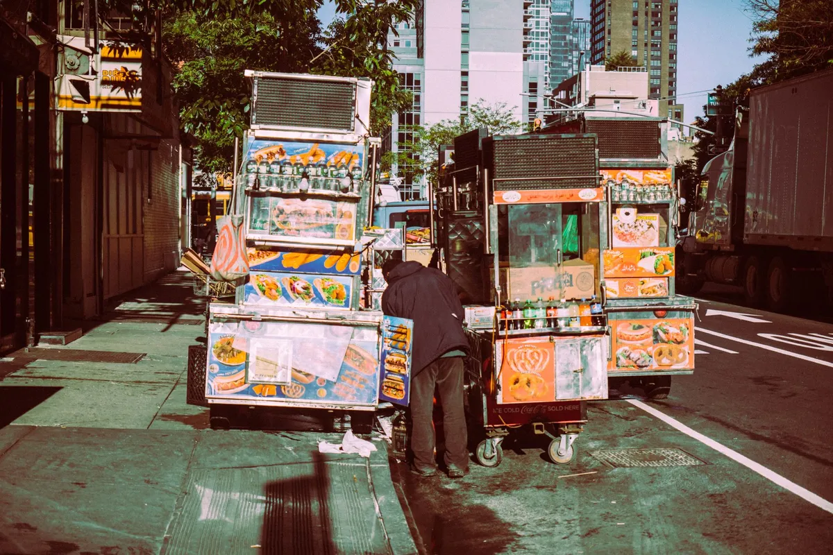 A black-and-white photograph of a 1920s street vendor pushing a cart filled with hamburgers