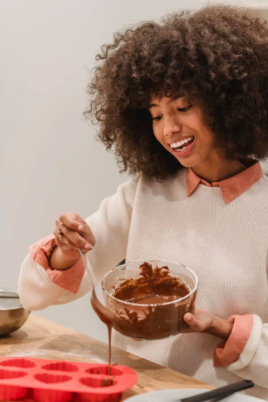 A chocolatier hand-pouring tempered chocolate into molds, with a focus on the glossy, flowing texture