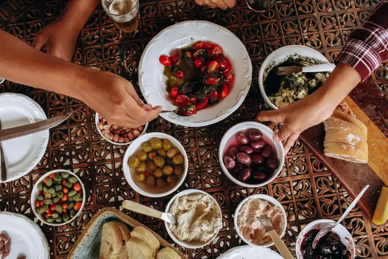 Famiglia felice condivide un pranzo mediterraneo all'aperto, con risate e cibo abbondante sotto il sole