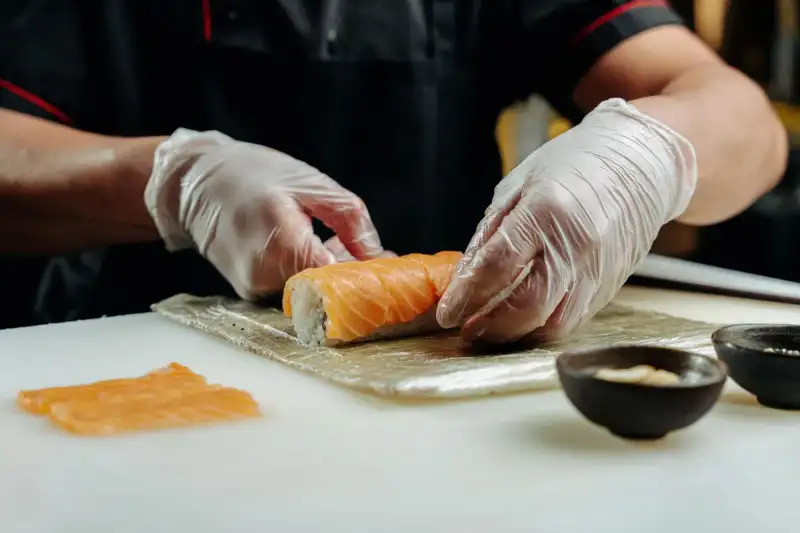 Mains expertes d'un chef japonais façonnant avec précision un nigiri sushi, mettant en évidence la dextérité et l'art derrière chaque pièce de ce plat emblématique.