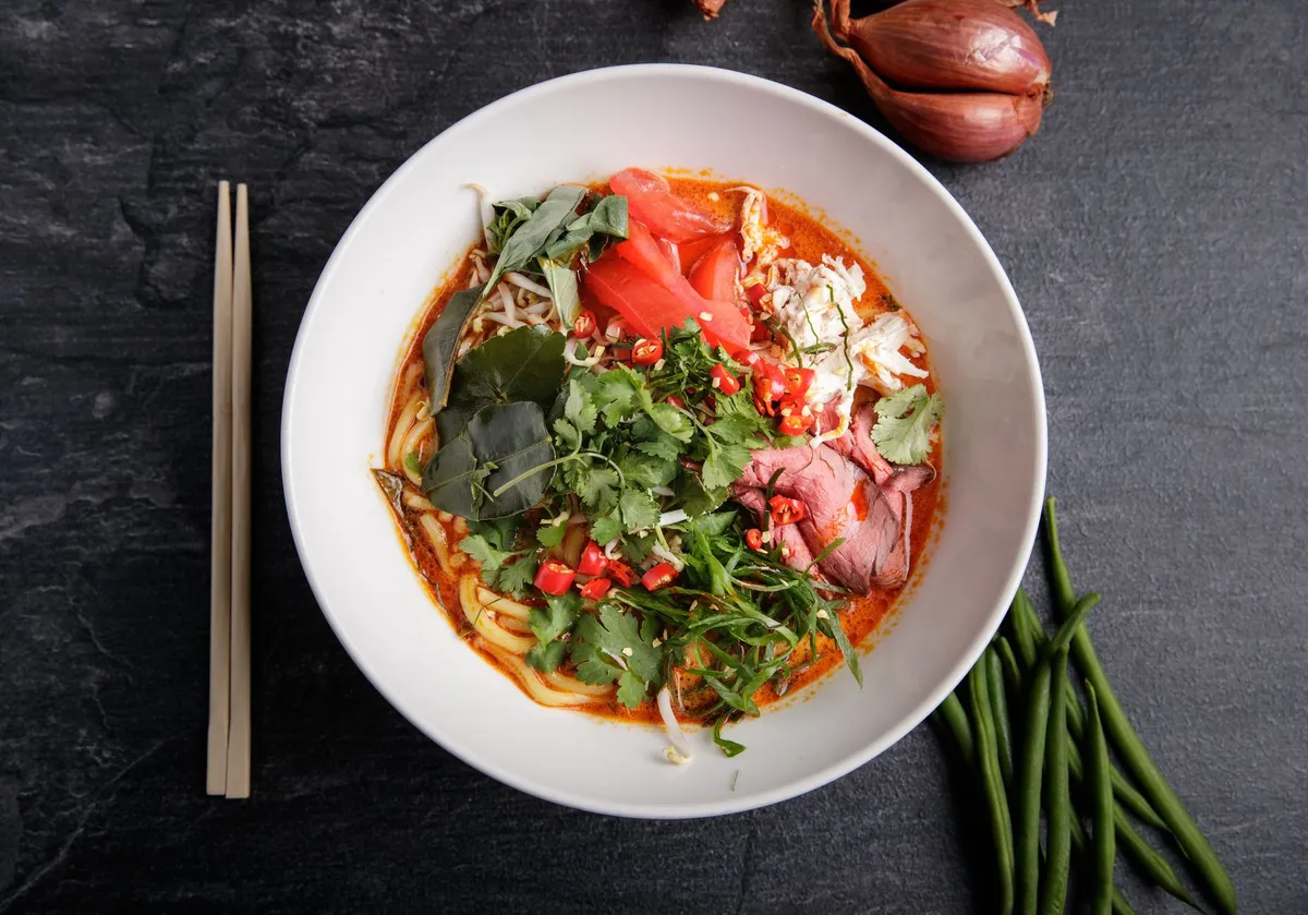 A bowl of Laksa with a side of vegetables