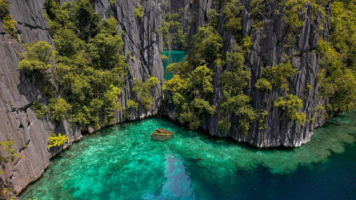 A group of travelers kayaking through a narrow lagoon passage with limestone cliffs on either side