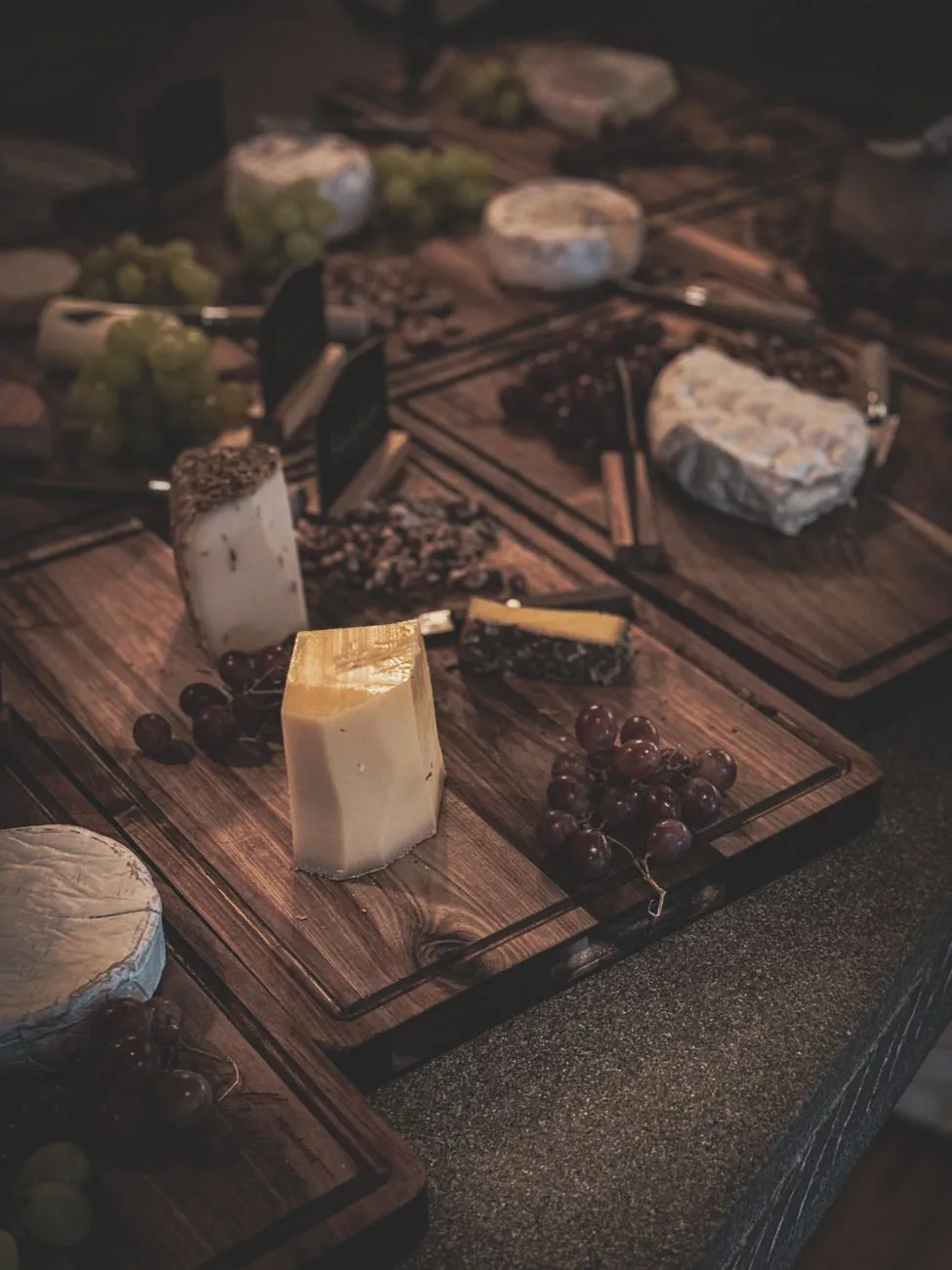 A rustic wooden table laden with a selection of French cheeses, a bottle of Bordeaux wine, and a baguette