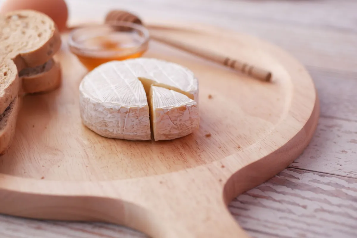 A wooden board displaying a variety of French cheeses, including Brie, Camembert, Roquefort, and Comté