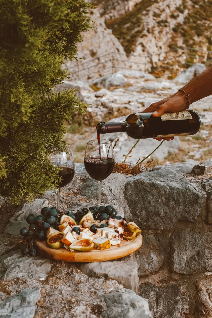 A close-up of a glass of red wine being poured next to a slice of cheese