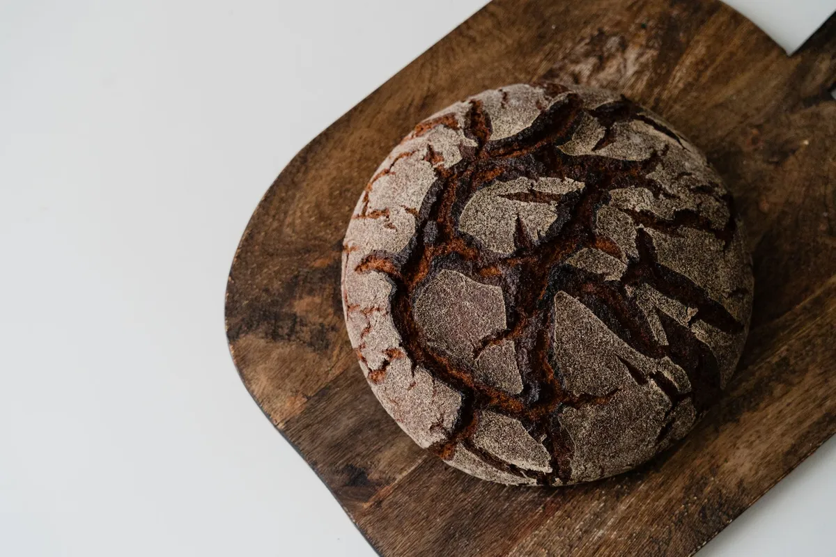 A golden-brown sourdough loaf with a crisp crust, resting on a wooden cutting board