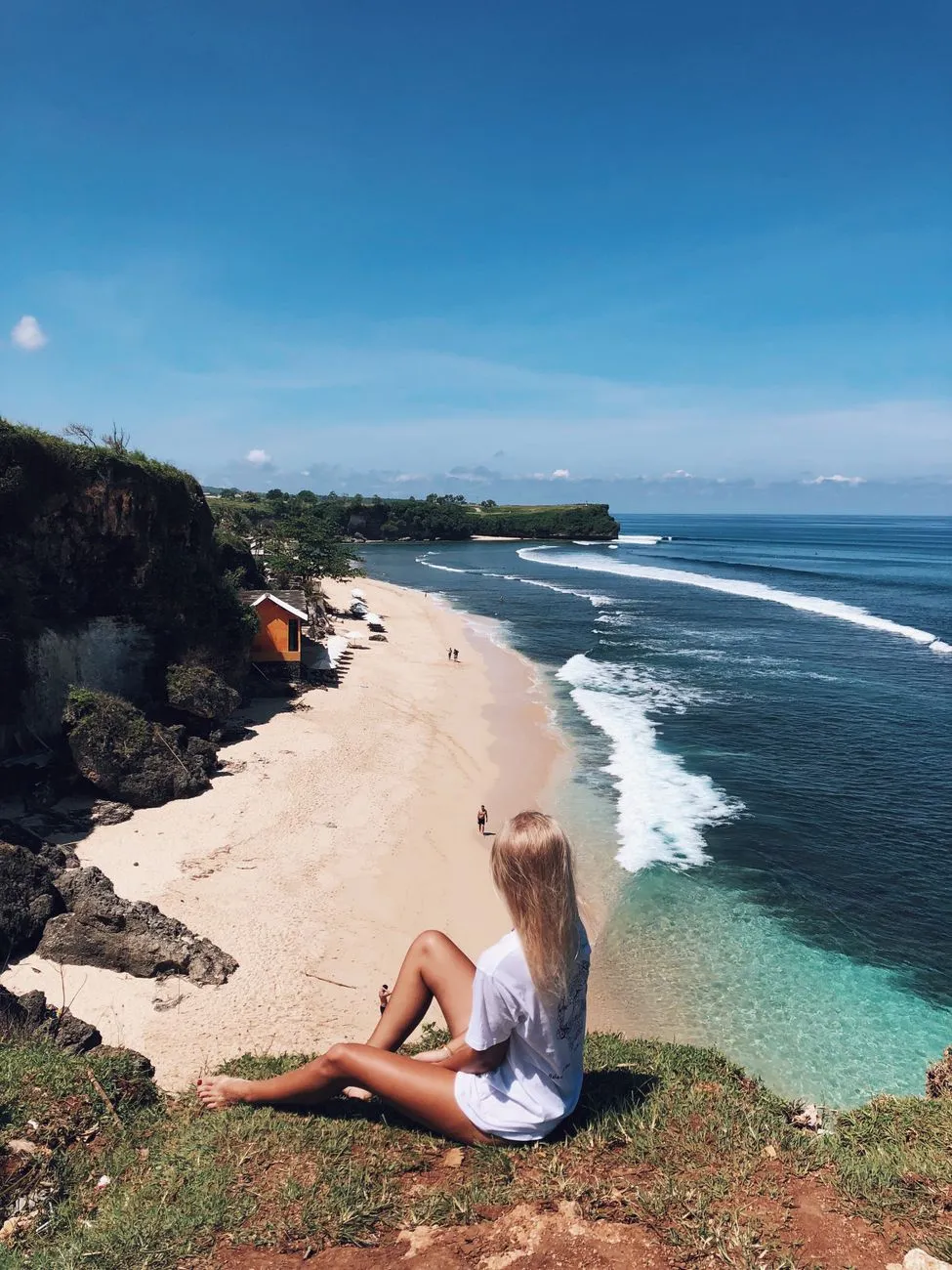 A traveler sitting on a cliff overlooking a pristine beach, holding a reusable water bottle