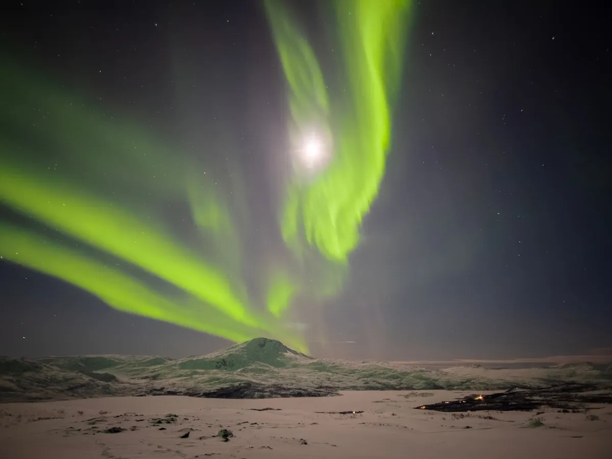 Aurora borealis over snowy mountains with cabin