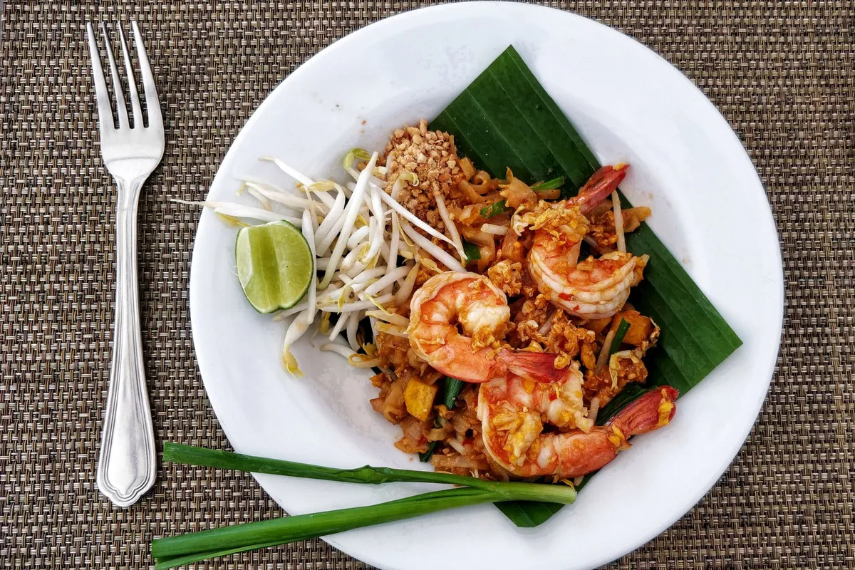A plate of pad thai topped with crushed peanuts, bean sprouts, and lime wedges
