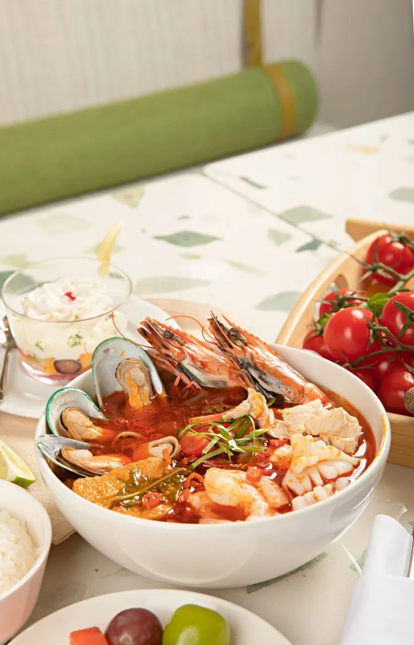 A bowl of tom yum goong with shrimp, lemongrass, and lime wedges