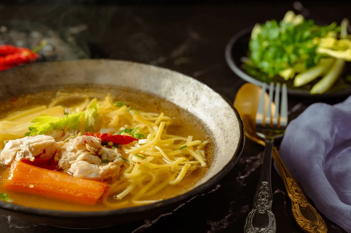 A bowl of khao soi with egg noodles, chicken, and crispy fried noodles on top