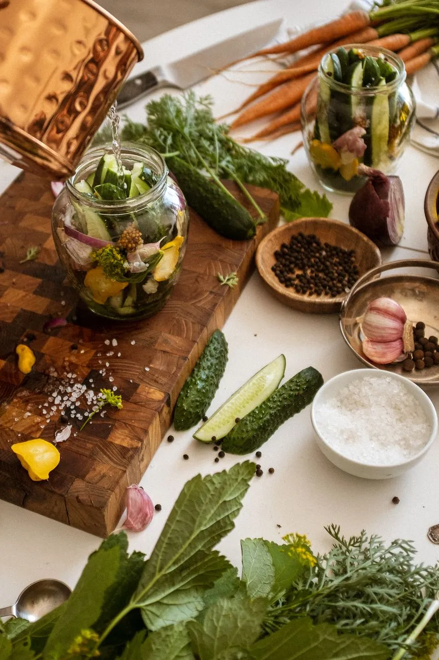 A wooden table scattered with jars of fermenting vegetables, a SCOBY, and a bottle of fizzy kefir