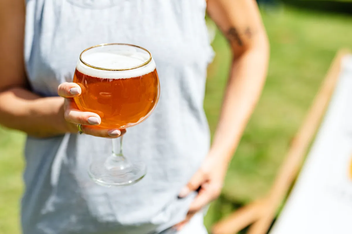 A person holding a glass of golden kombucha, with a SCOBY floating in the background