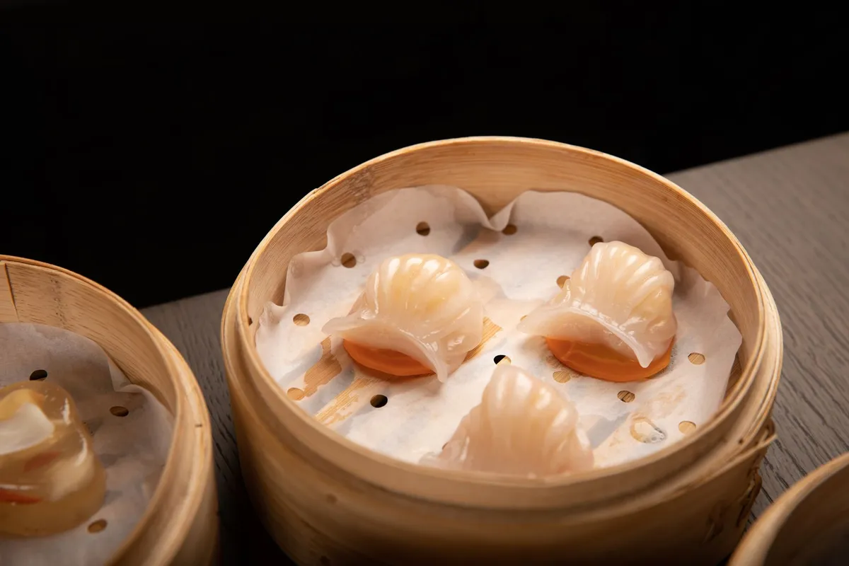 A close-up of a hand holding a har gow dumpling