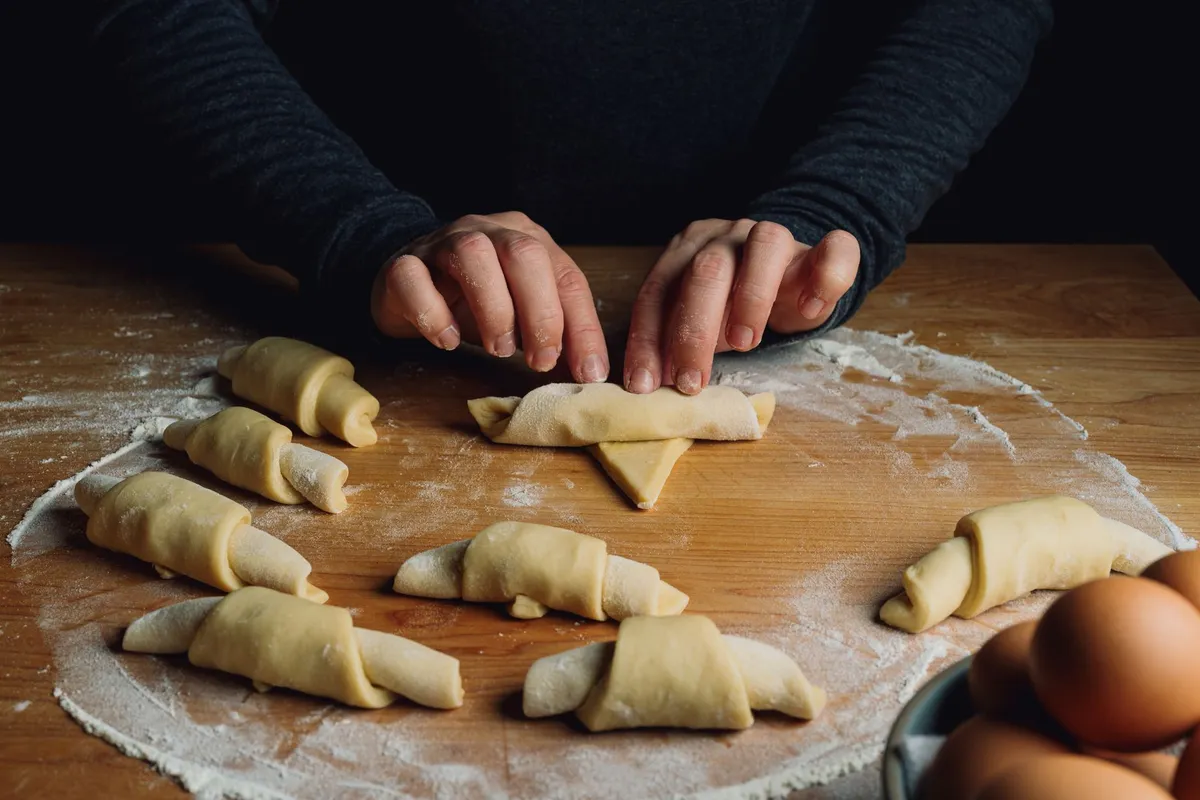 A close-up of a baker's hands rolling out laminated dough for croissants