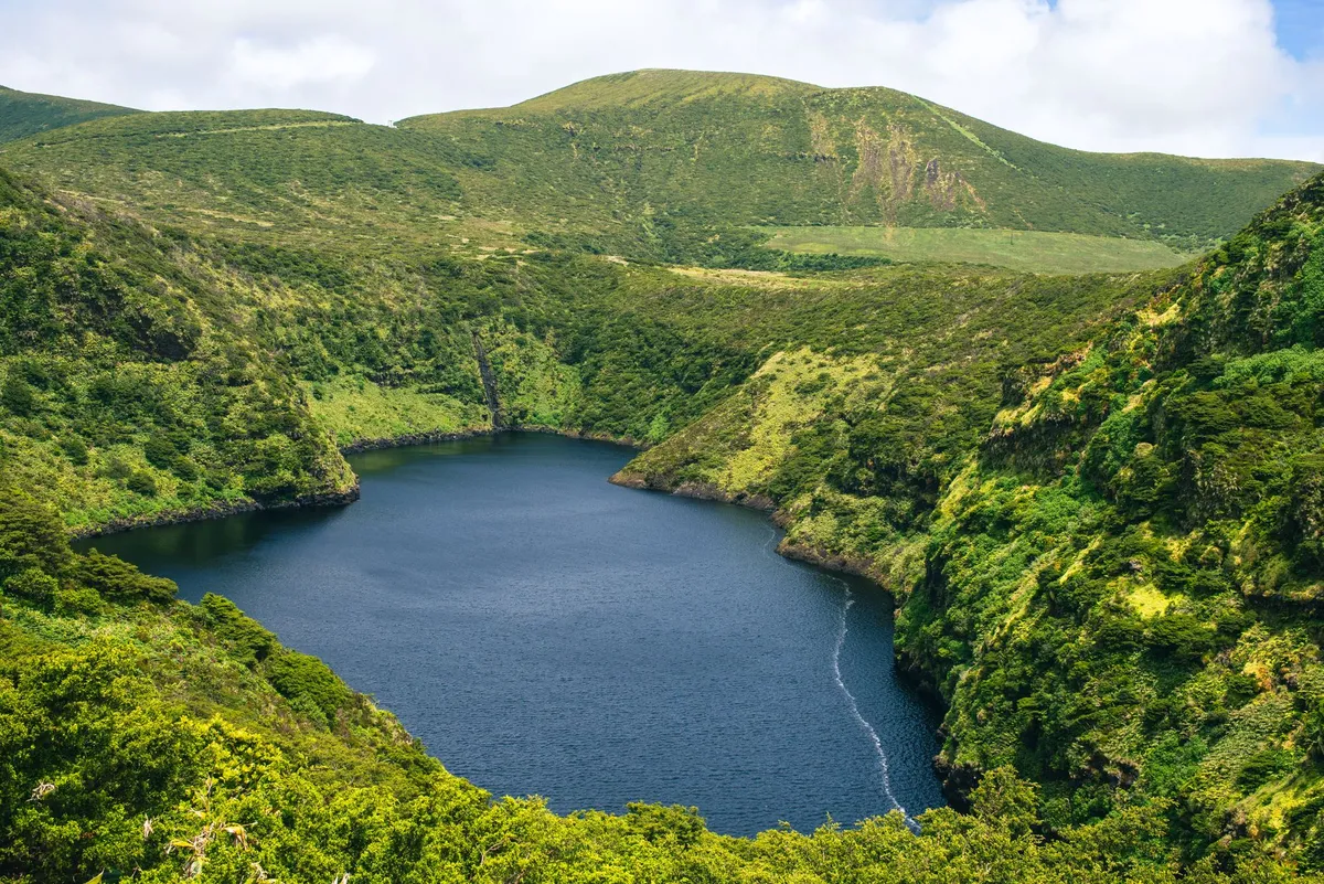Aerial view of a volcanic crater lake surrounded by lush green hills