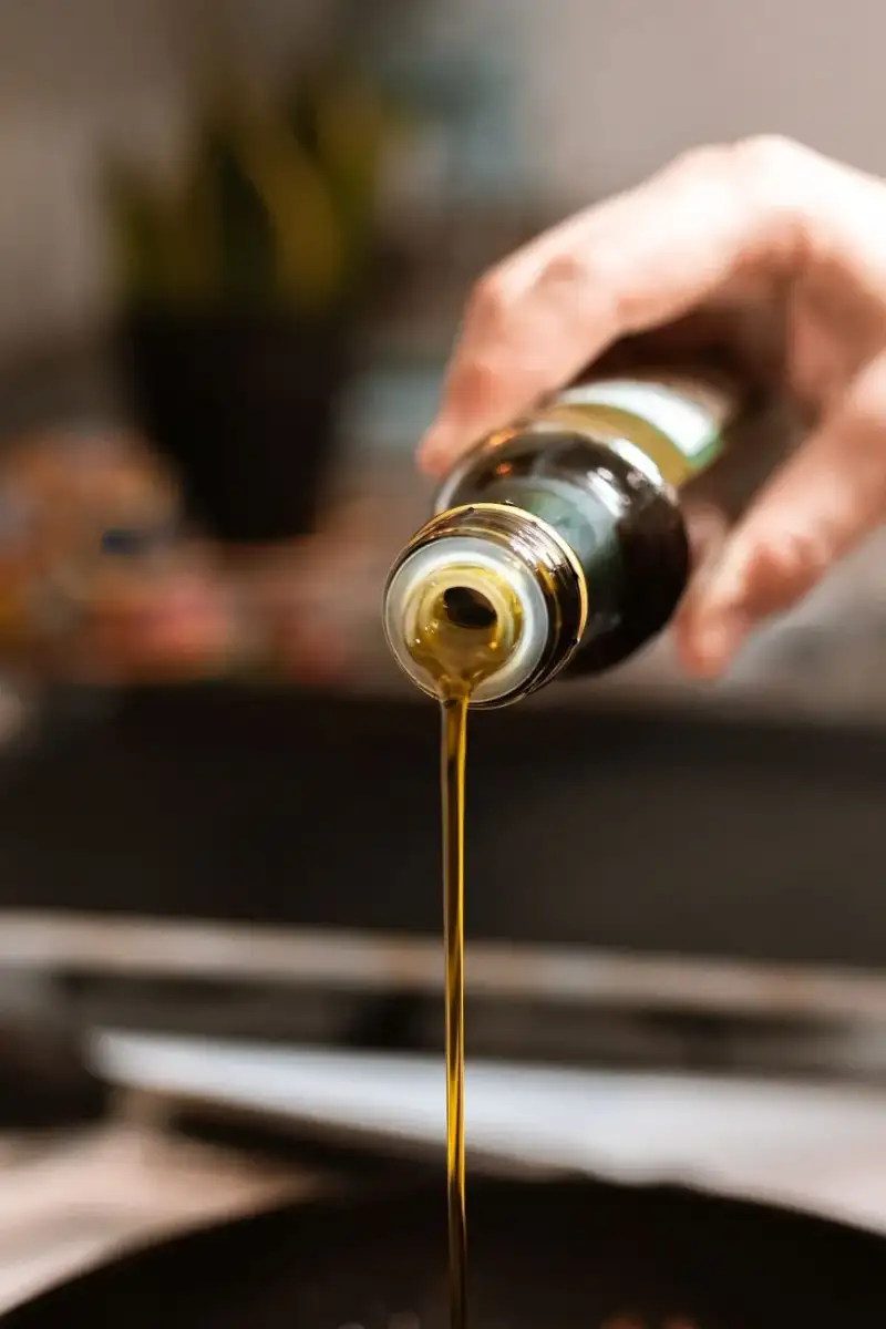 A stream of golden olive oil being poured over fresh salad greens
