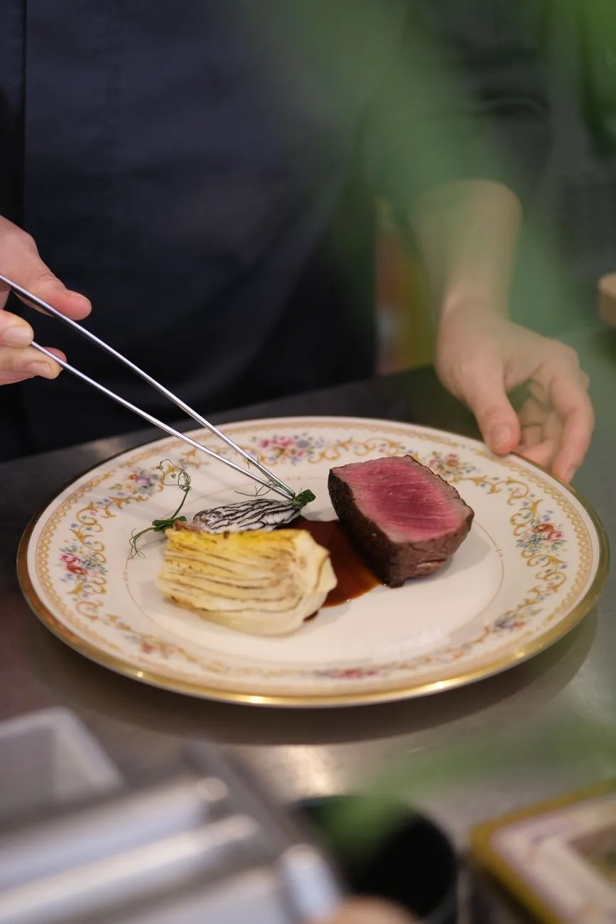 Chef finishing a dish with a sprinkle of seasoning over a steaming bowl of ramen