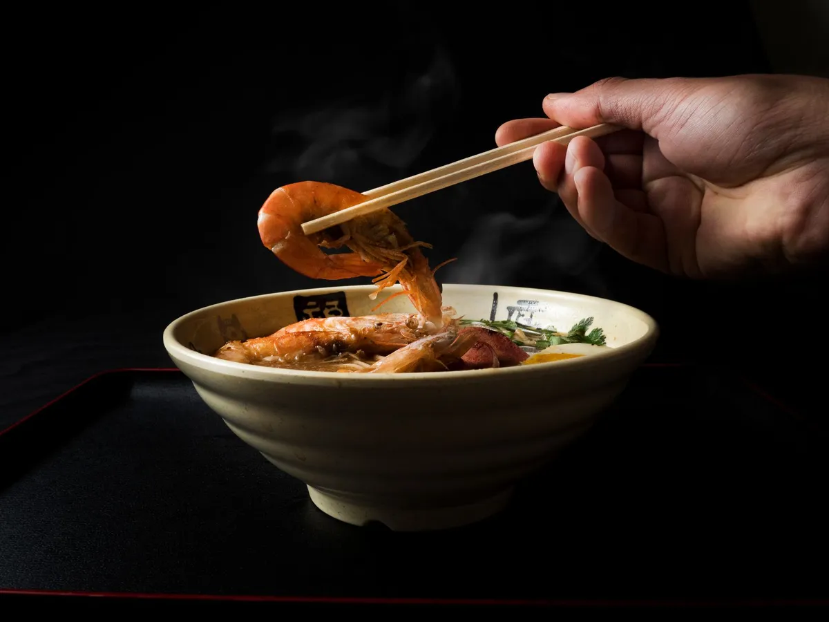 A person sniffing a bowl of hot ramen, illustrating the role of olfaction in taste perception