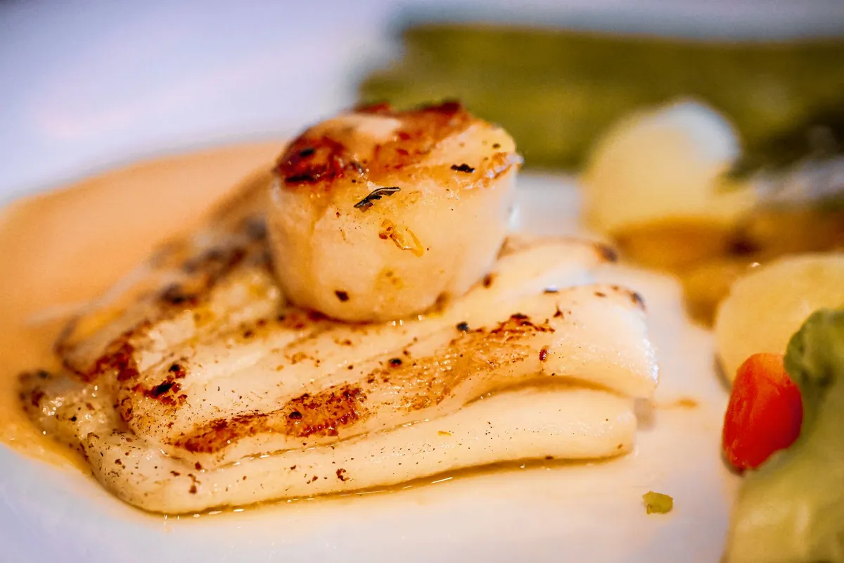 A chef sprinkling flaky sea salt over a perfectly seared scallop, demonstrating the final touch of umami enhancement