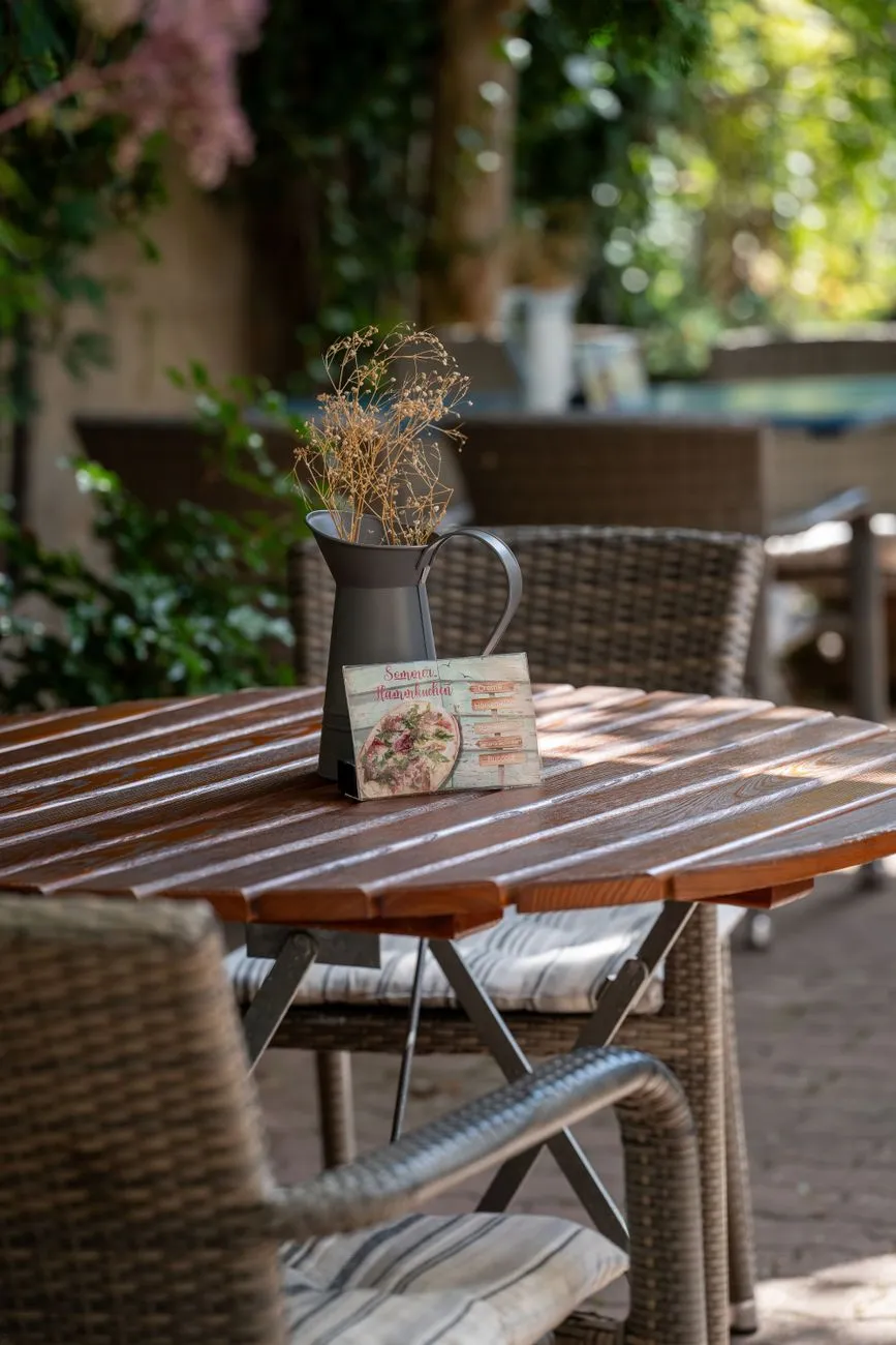 A rustic wooden table set with homemade bread, local cheese, wine, and olives in a sunlit courtyard