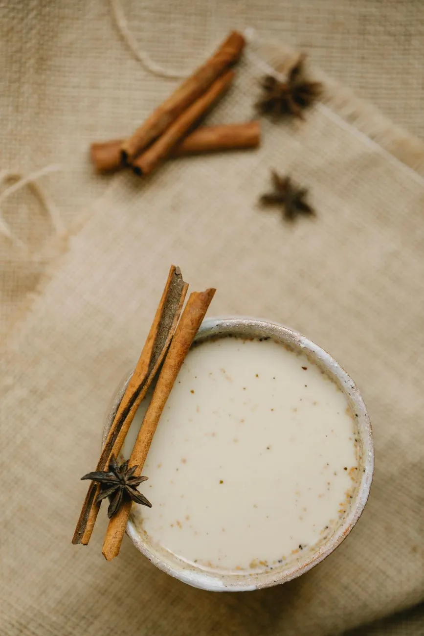 A steaming clay cup of masala chai with cinnamon sticks, cardamom pods, and ginger slices floating on the surface