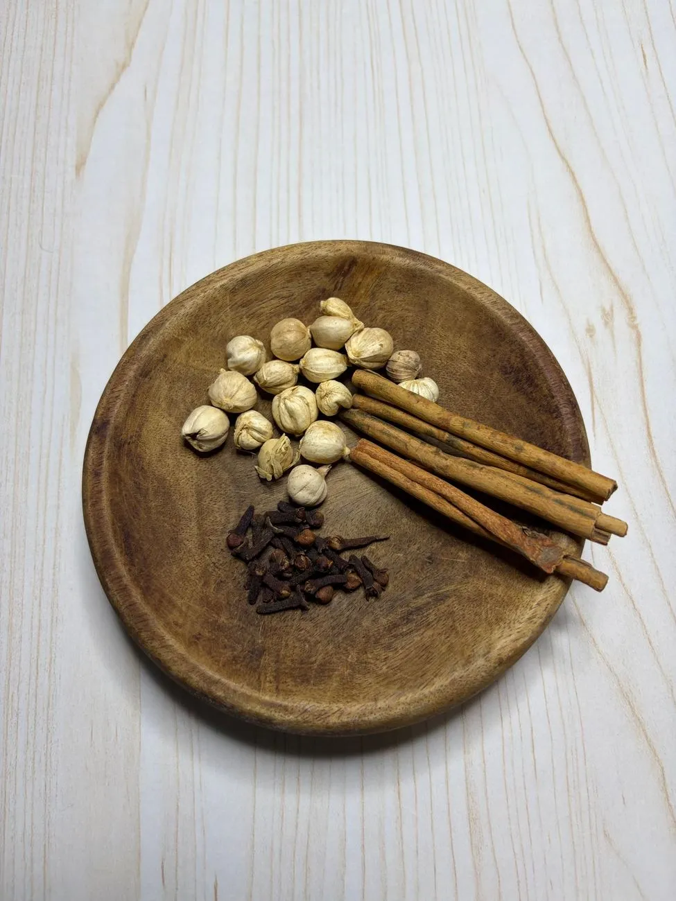 A wooden mortar and pestle filled with whole spices—cardamom, cloves, cinnamon, and black pepper—ready to be ground for chai