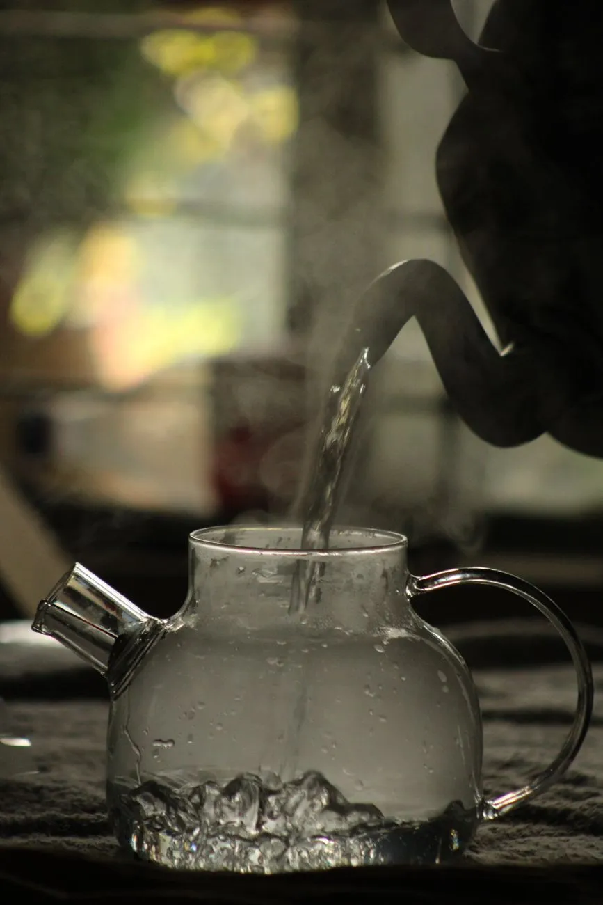 A brass or stainless steel kettle boiling water with loose black tea leaves and spices, steam rising dramatically