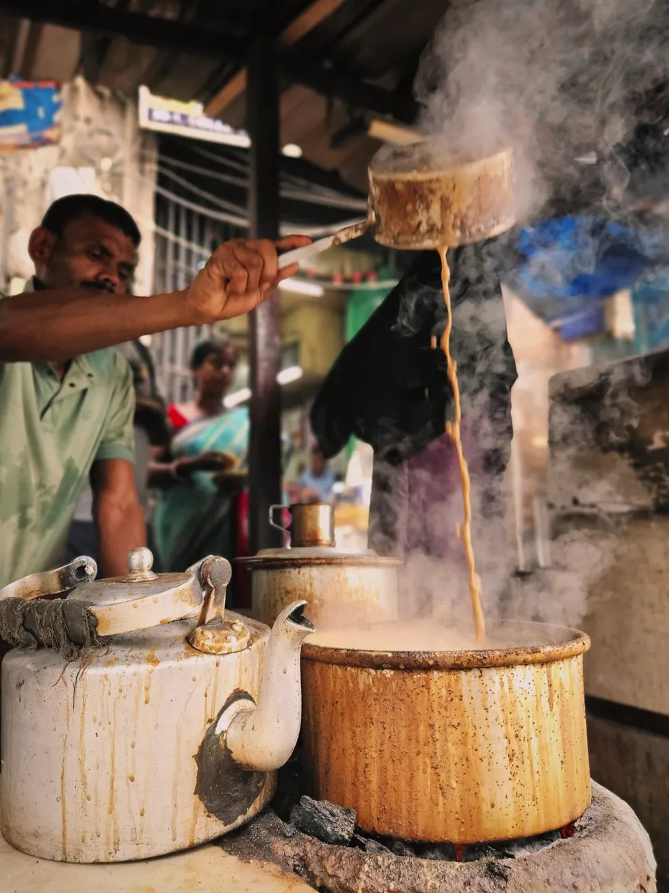 A street vendor in Varanasi pouring freshly brewed chai from a brass kettle into small clay cups