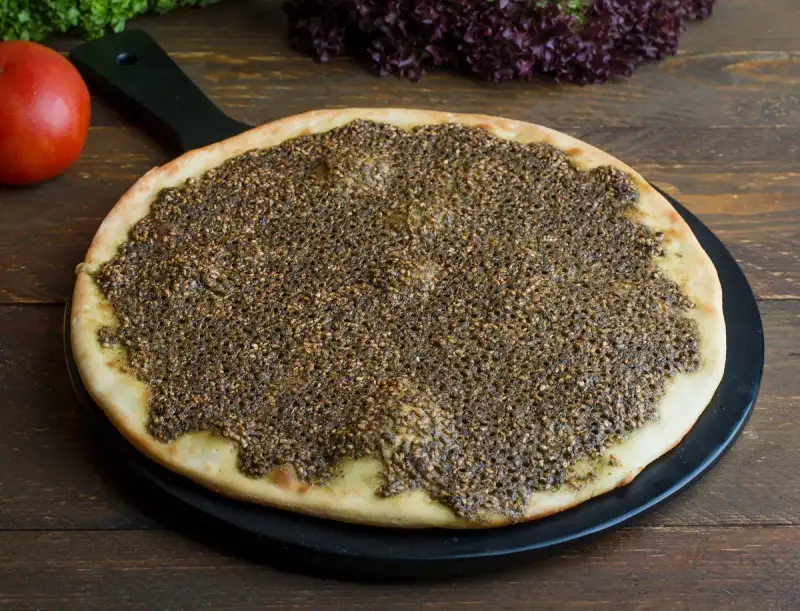 Close-up of a bowl of vibrant green za'atar spice blend, ready to be sprinkled over hummus.