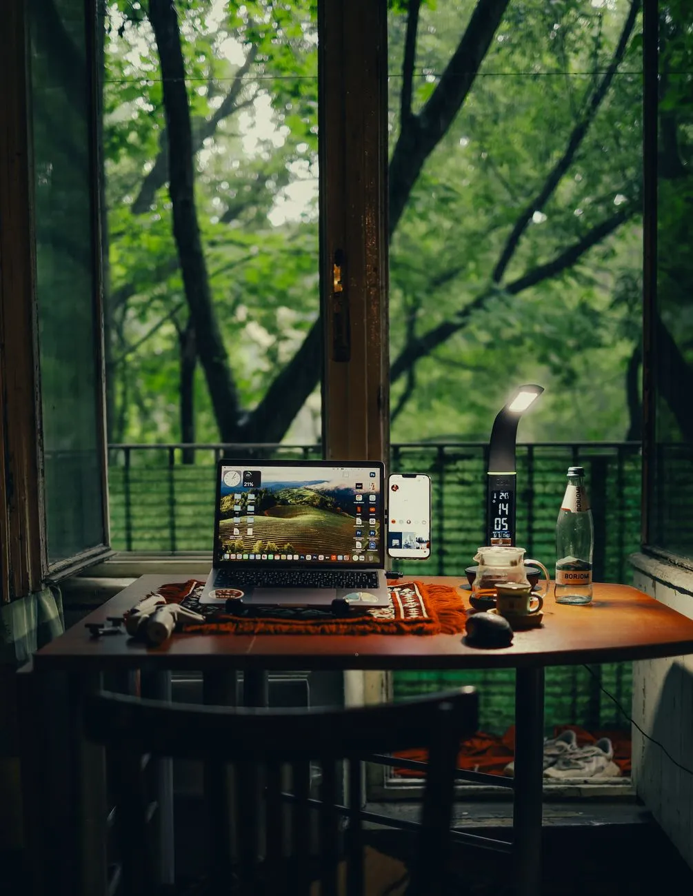 A sleek laptop set up on a rustic wooden desk with a massive window overlooking a vast, snow-covered Icelandic mountain range.