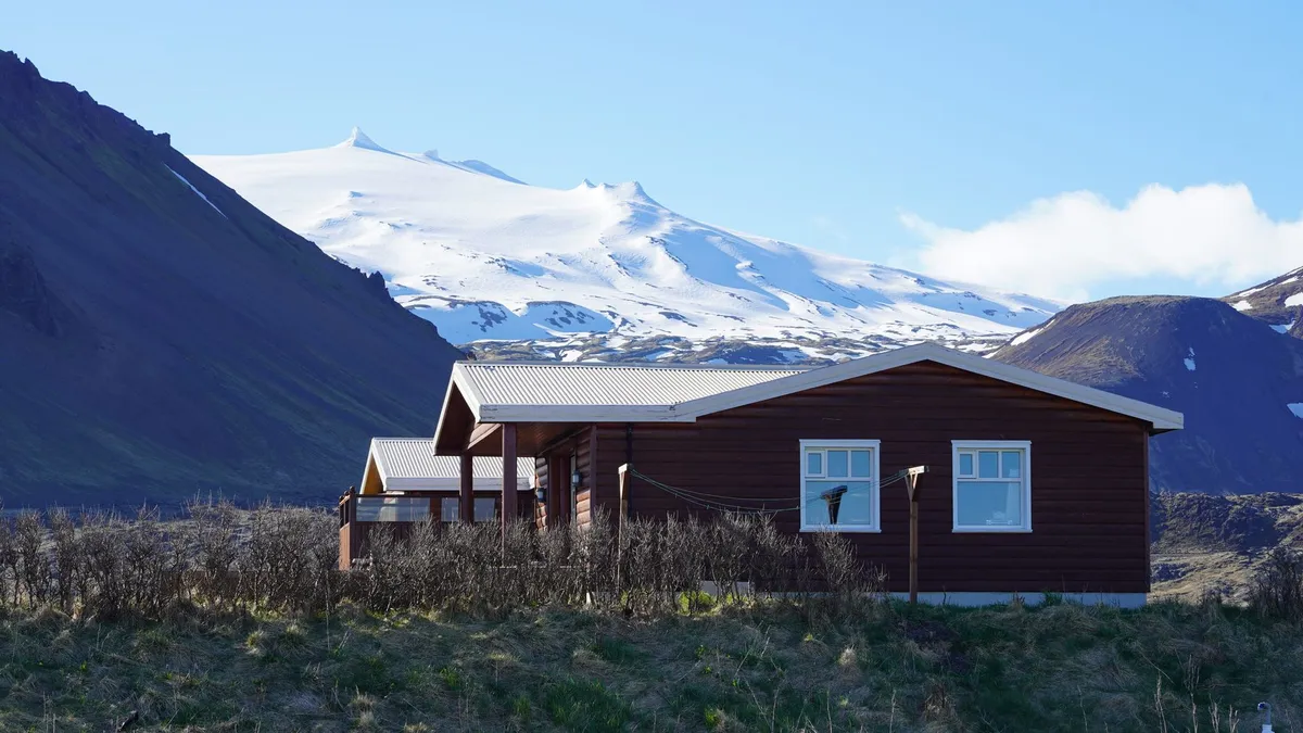 A person wrapped in a wool blanket sitting on a porch deck facing an Icelandic geothermal field during twilight.