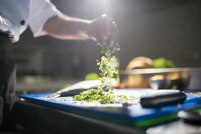 A close-up of vibrant, fresh green herbs, garlic cloves, and sliced carrots on a wooden cutting board