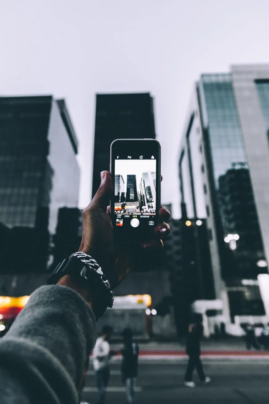 A person holding a smartphone with a distorted reflection of a city skyline