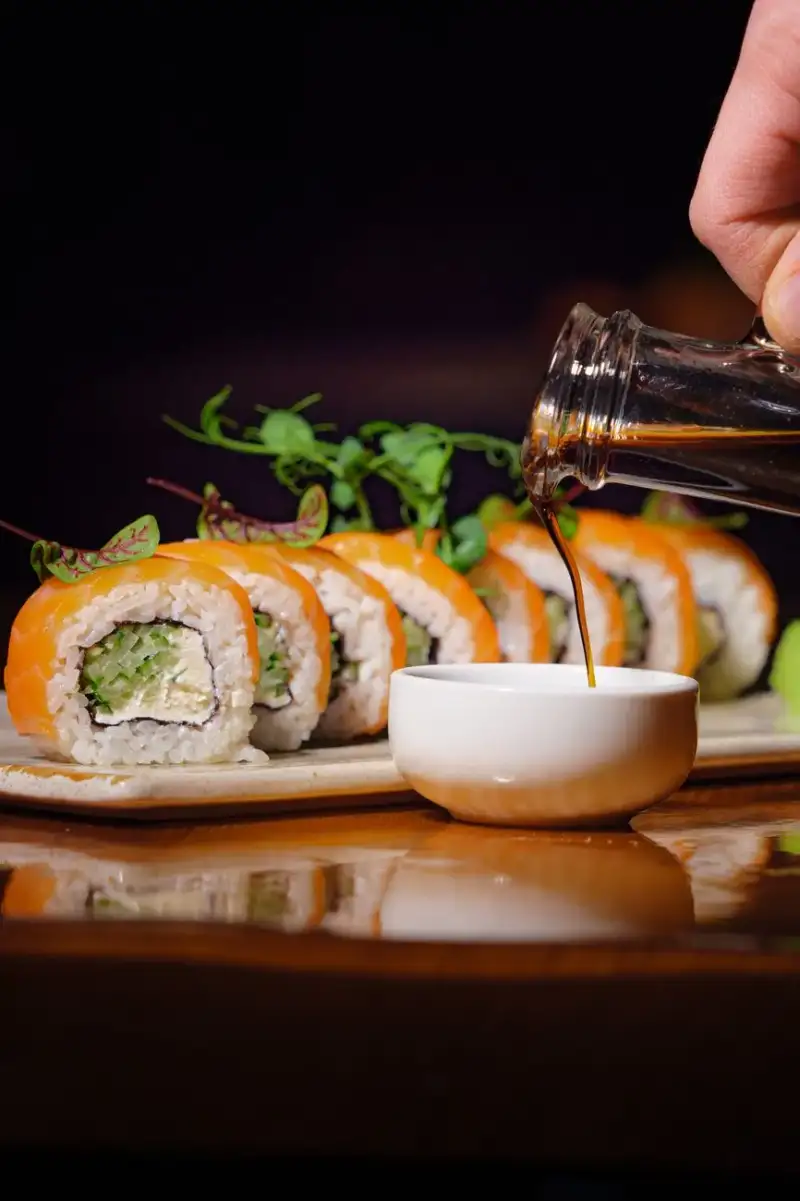 A close-up of a chef drizzling soy sauce over a dish, highlighting the deep, savory essence of umami