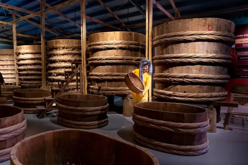A wooden barrel filled with fermenting soybeans, with a chef stirring the mixture
