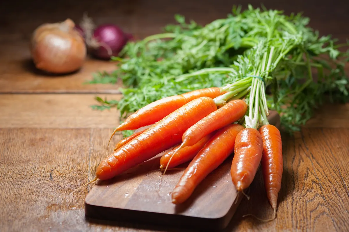 Carrot tops being chopped on a wooden board